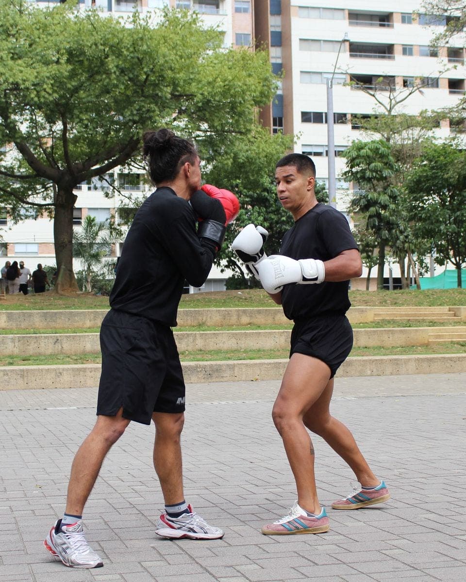 Dos personas hacen sparring con guantes en un parque.